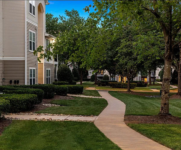 Charming apartment complex with beautifully landscaped paths and lush green trees creating a peaceful neighborhood ambiance.