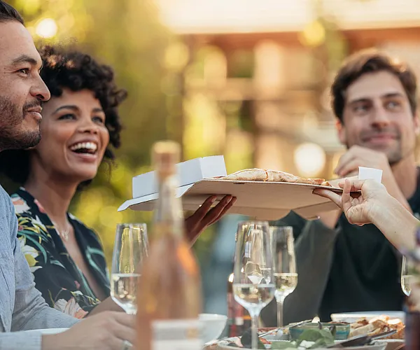 Joyful group of friends sharing pizza and wine outdoors, surrounded by a warm and inviting atmosphere.