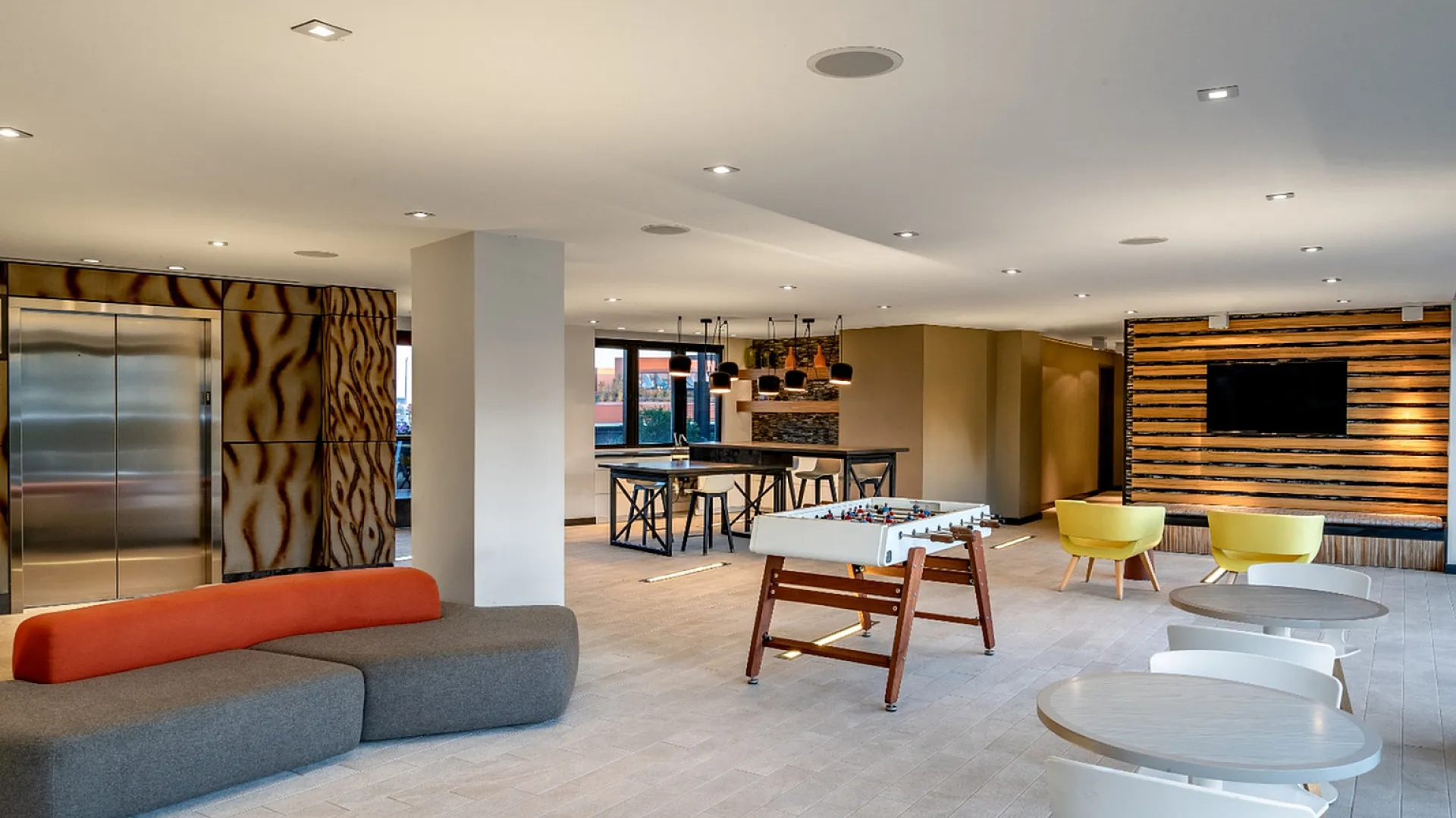 Contemporary open-plan living space with chic decor, featuring a cozy seating area, stylish dining setup, and modern foosball table.