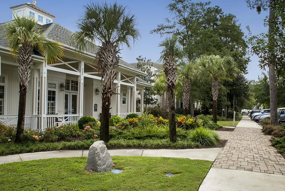 Charming residential building surrounded by lush palm trees and vibrant gardens, offering a tranquil setting with convenient parking and a welcoming pathway.