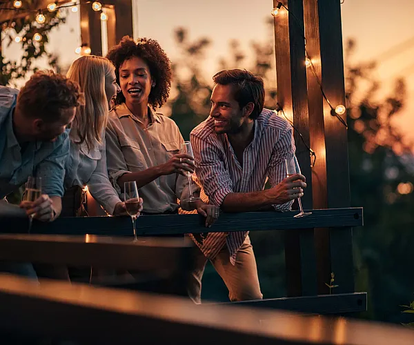 Charming sunset balcony gathering with friends enjoying wine under string lights, perfect for socializing and relaxation.