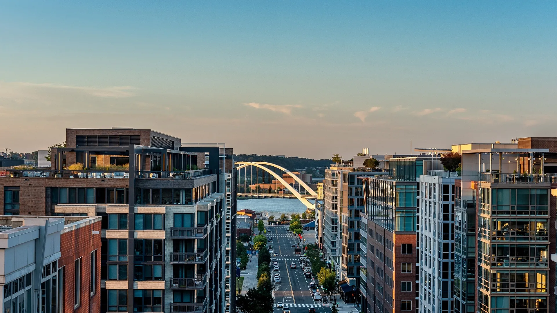 Sunset view of a vibrant urban street lined with modern apartments, featuring a stunning bridge in the background, offering a desirable city living experience.