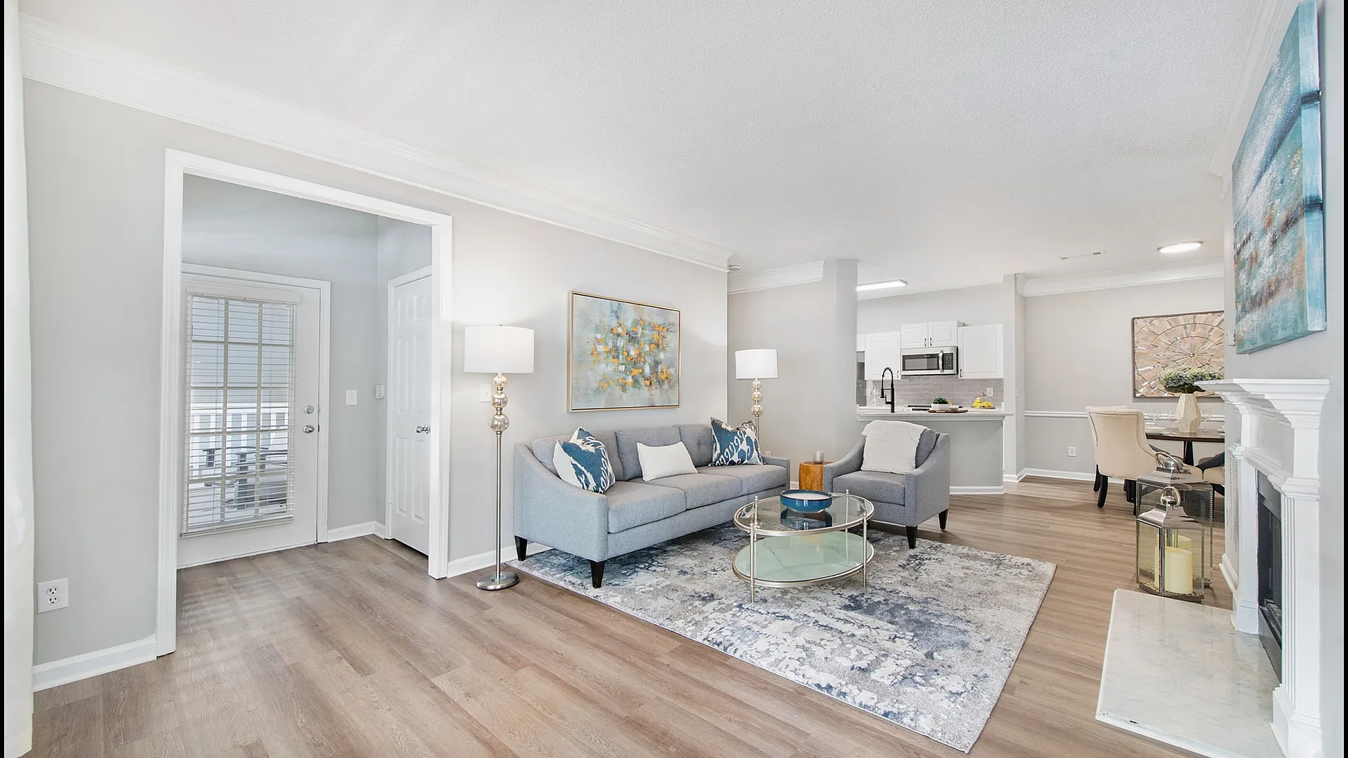 Inviting open-concept living room with modern decor, featuring a cozy sofa, stylish armchair, and contemporary artwork. Bright and airy space with a sleek kitchen and dining area in the background.