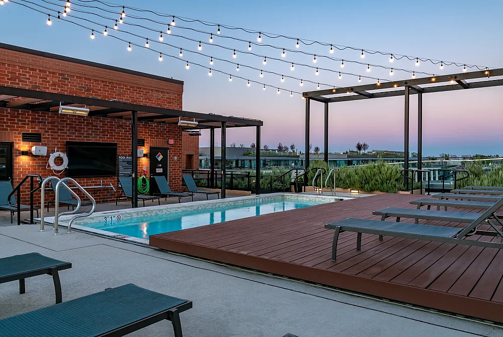 Charming rooftop pool area with ambient string lights and stylish lounging chairs, offering stunning sunset views.