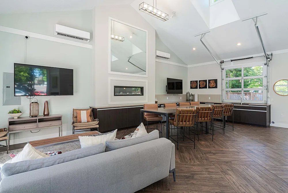 Bright and modern living area with high ceilings, chic decor, ample seating, and a wall-mounted TV, perfect for entertaining.