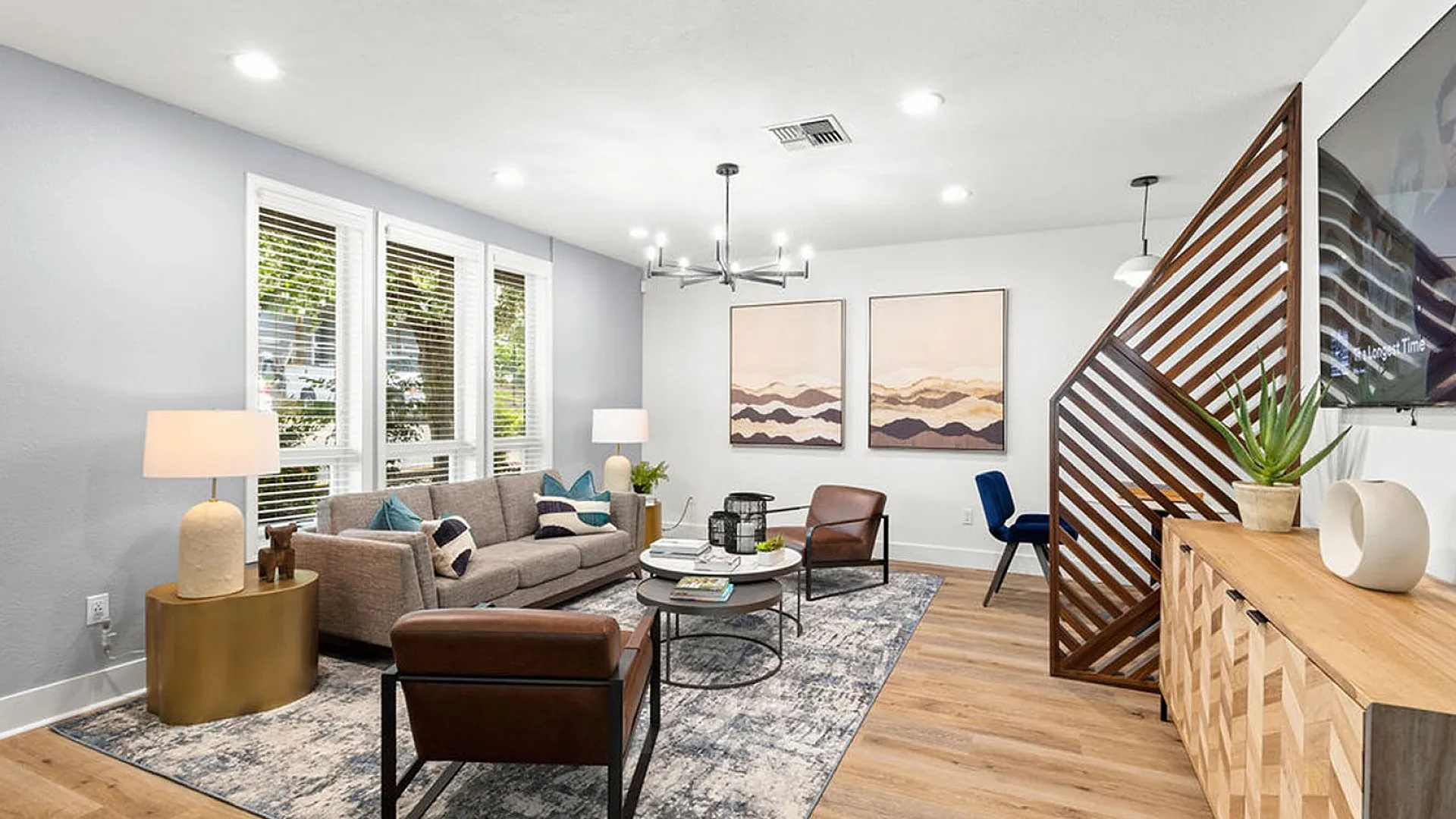 Modern living room featuring a cozy gray sofa, accent chairs, and a stylish wooden divider with geometric art and lush greenery.