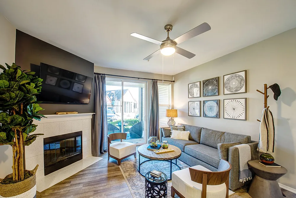 Modern and inviting living room featuring a cozy fireplace, stylish gray sofa, and wall art with elegant patterns. Bright and airy with natural light streaming through large windows, creating a warm and welcoming ambiance.