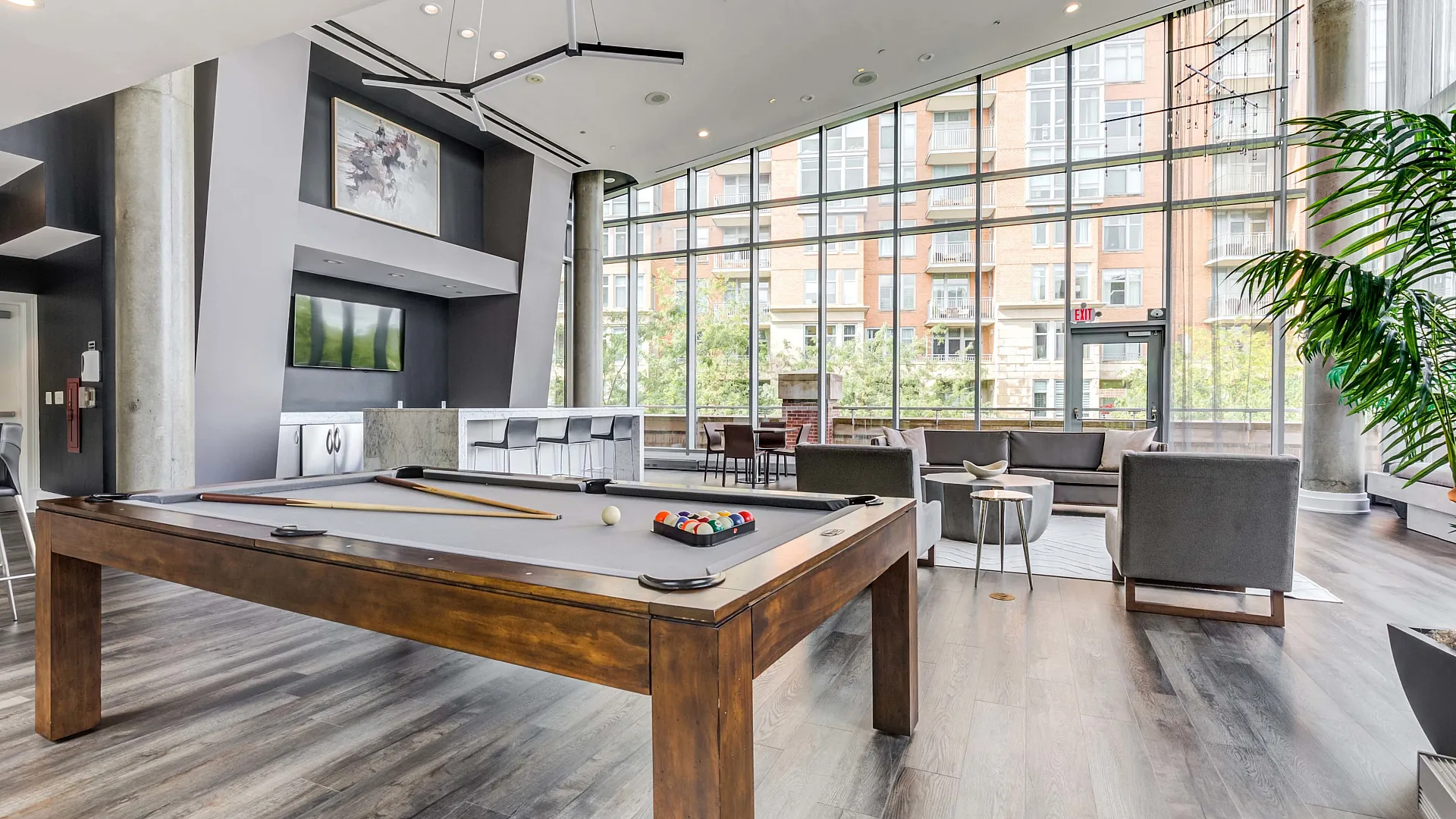 Contemporary apartment lounge with floor-to-ceiling windows, featuring a stylish billiard table and modern seating area for socializing.