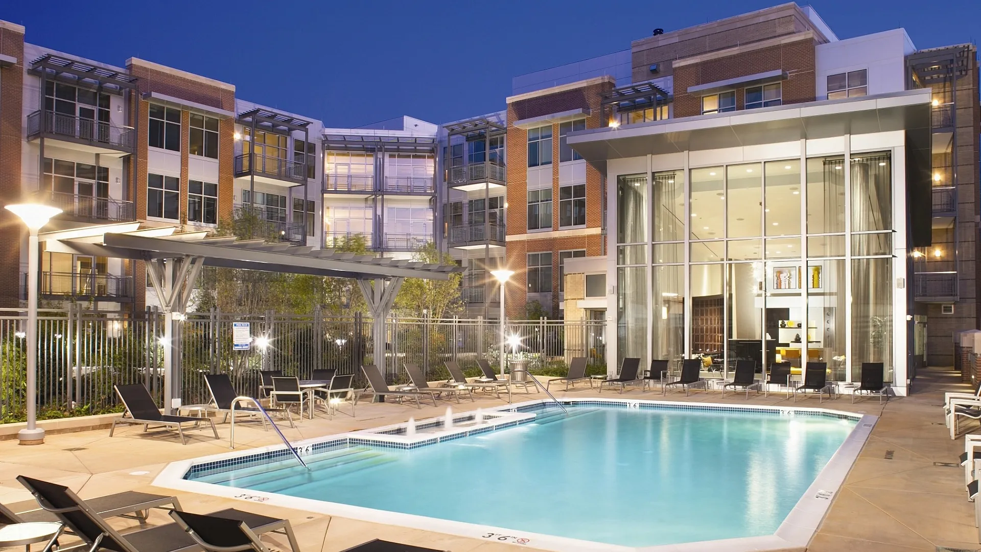 Luxurious apartment complex with a sparkling pool, modern architecture, and ambient evening lighting, perfect for sophisticated urban living.