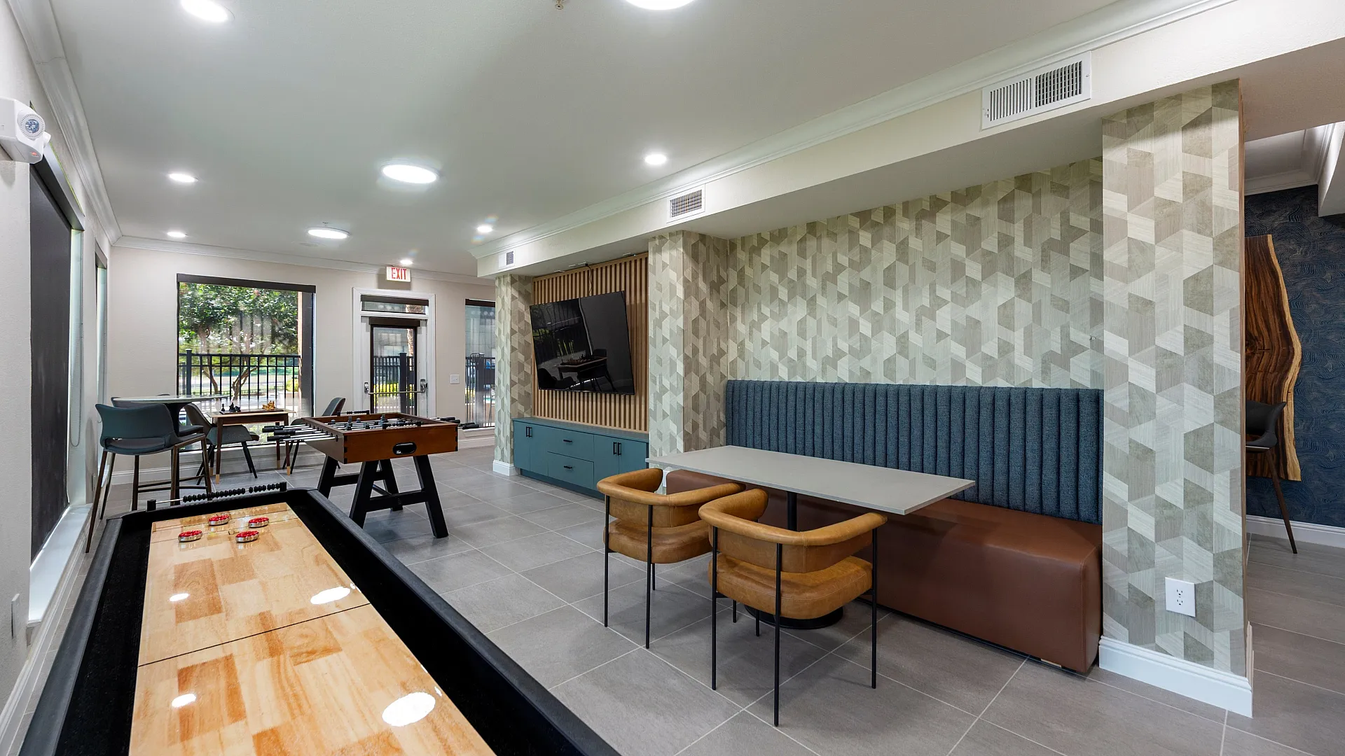 Contemporary entertainment room featuring sleek shuffleboard and foosball tables, modern seating, and stylish geometric wallpaper.