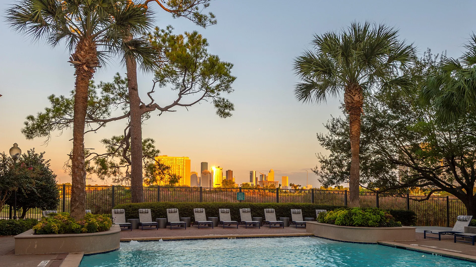 Luxurious pool area with palm trees overlooking a stunning city skyline at sunset, perfect for relaxation and leisure.