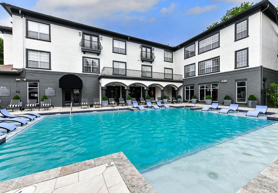 Elegant apartment complex with a luxurious outdoor pool, sun loungers, and modern architecture.