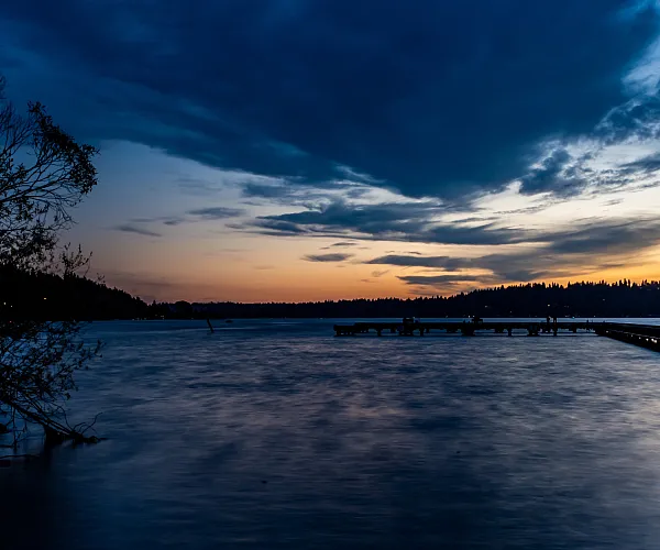 Serene sunset over a tranquil lake with silhouetted trees and an inviting dock, perfect for peaceful waterfront living.