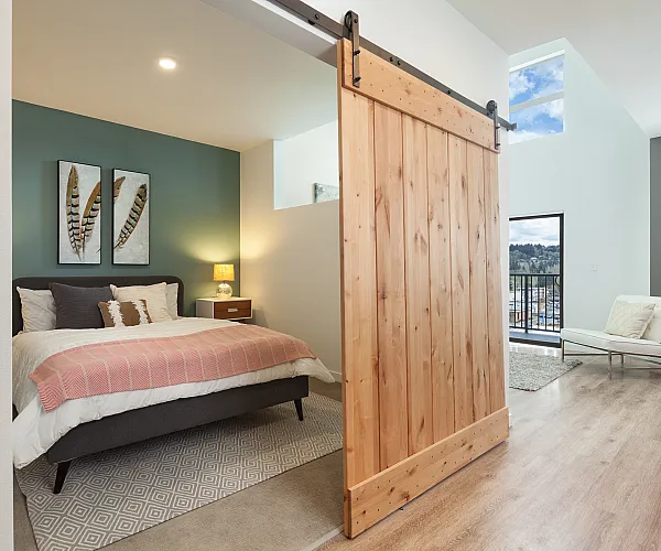 Cozy bedroom with elegant barn door, featuring stylish d&eacute;cor, soft lighting, and a serene balcony view.