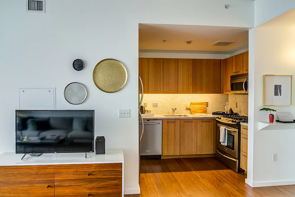 Contemporary open-plan living room and kitchen with sleek wooden cabinetry, modern appliances, and artistic decor accents.
