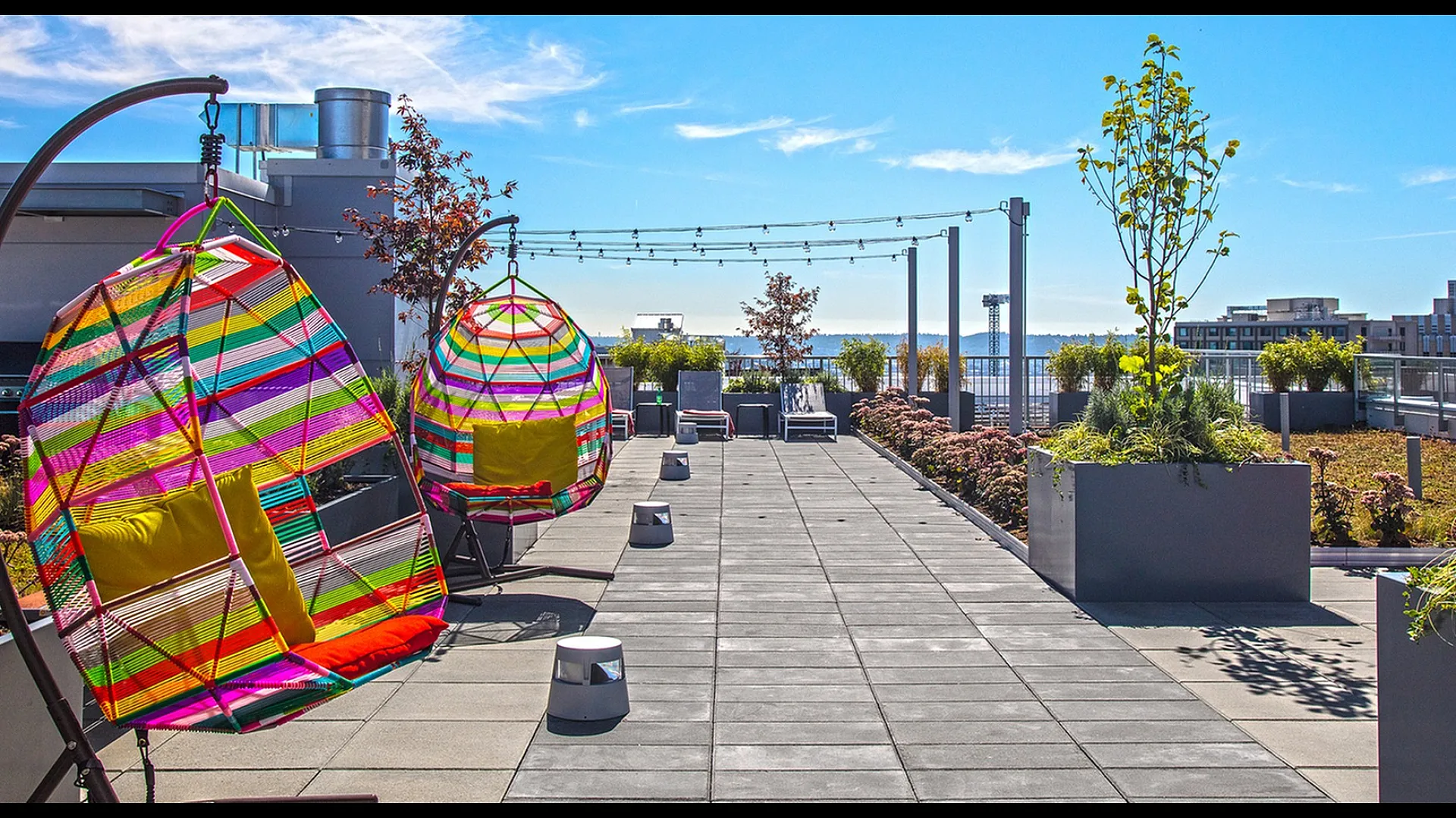 Vibrant rooftop terrace with colorful hanging chairs, lush greenery, and stunning city skyline views.