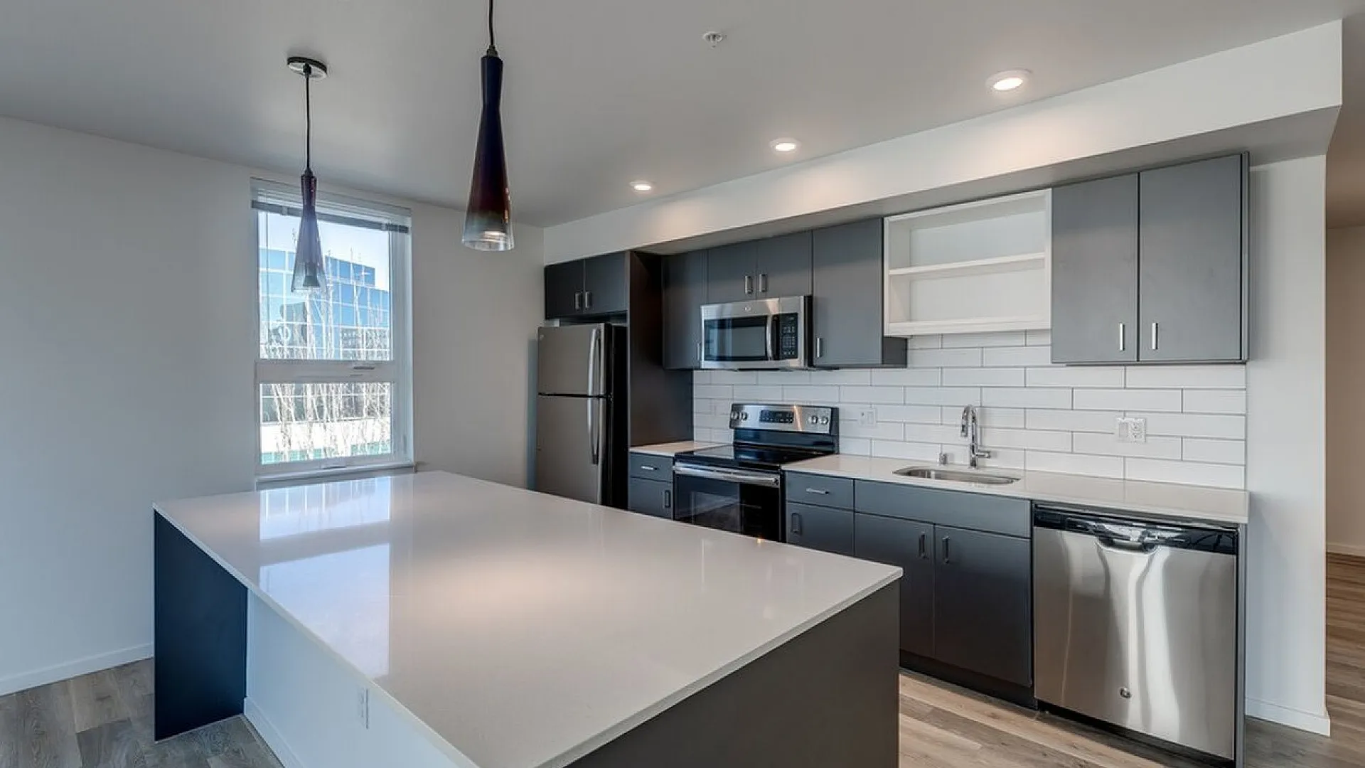 Modern kitchen with sleek dark cabinetry, stainless steel appliances, and elegant pendant lighting over a spacious white island.