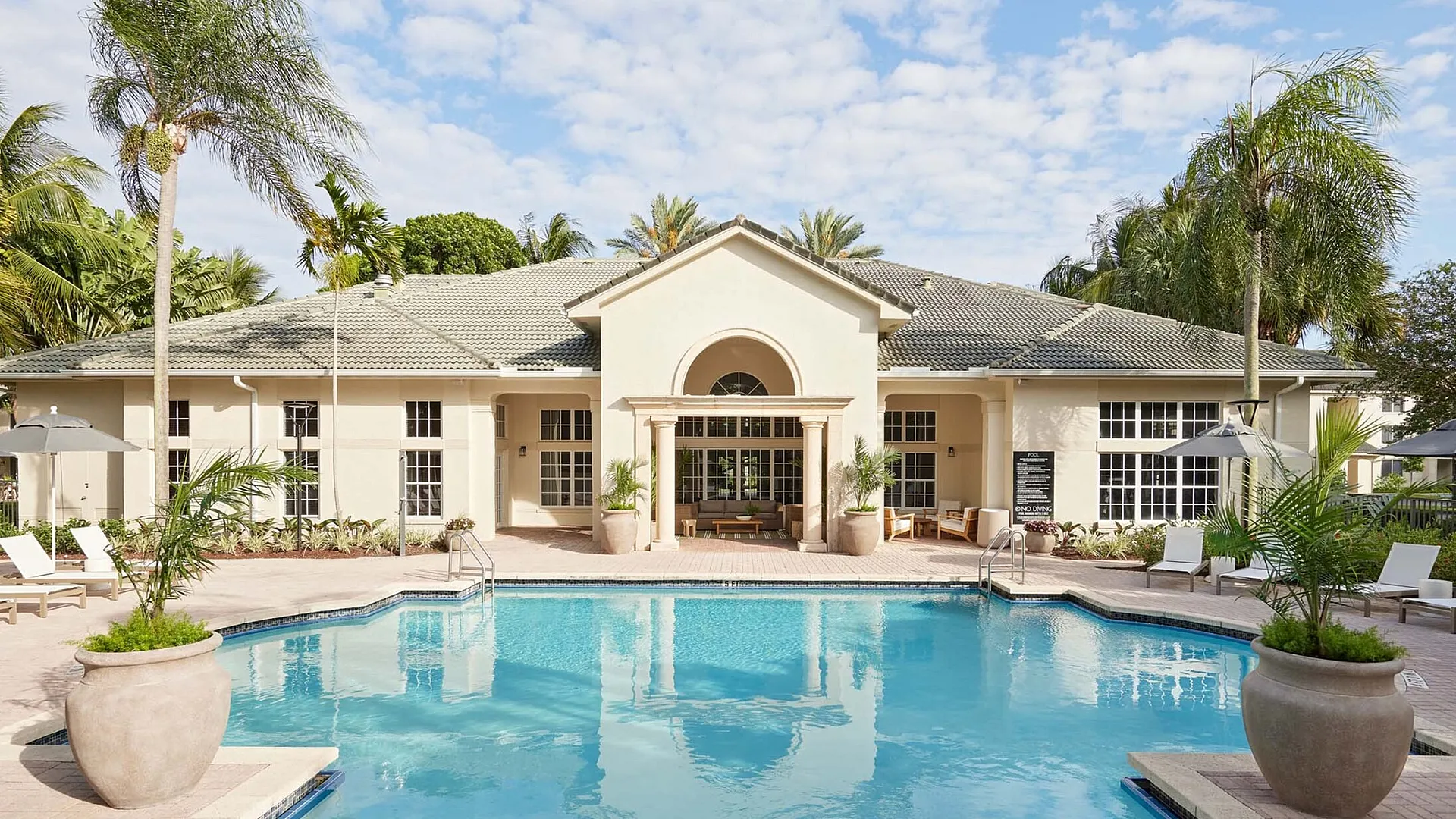 Luxurious apartment complex with a pristine swimming pool, lush palm trees, and stylish outdoor seating for ultimate relaxation.