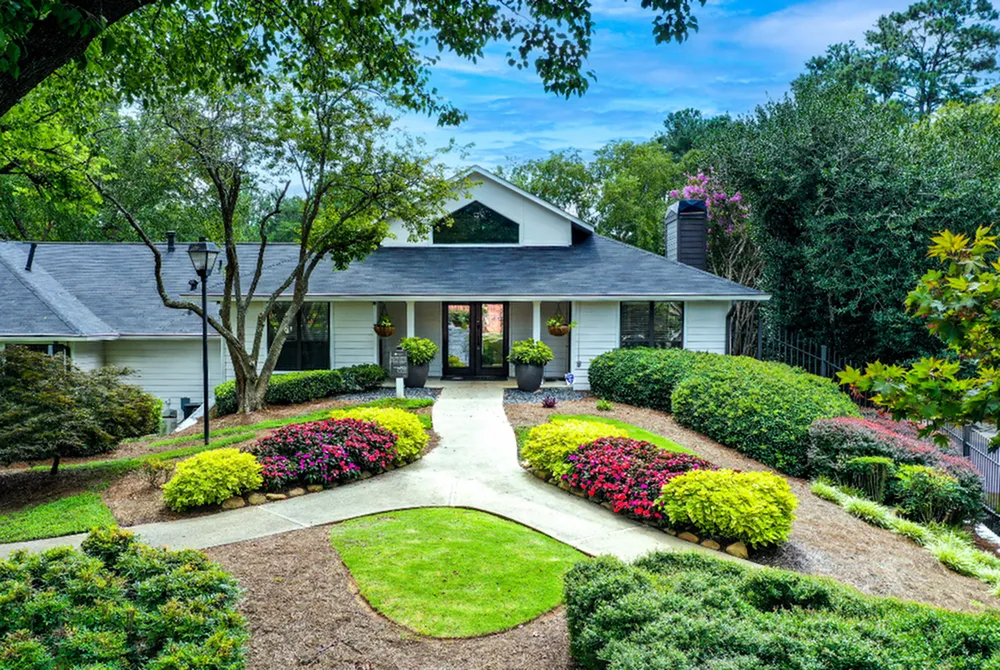 Charming single-story house with modern architecture, framed by lush greenery and vibrant flowers, creating a serene and welcoming entrance.