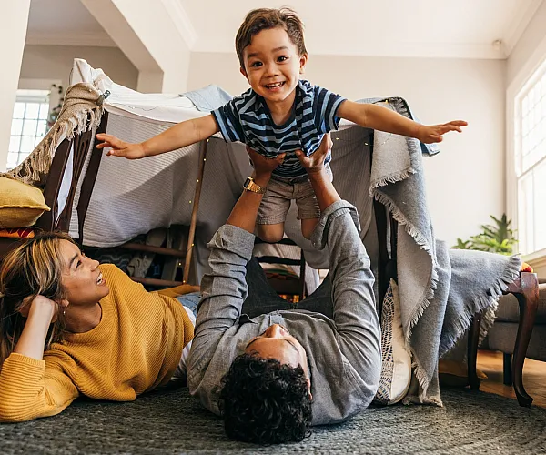 Cozy and inviting living room scene with a family enjoying a playful moment in a blanket fort. Natural light floods the space, highlighting the warm, cheerful ambiance.