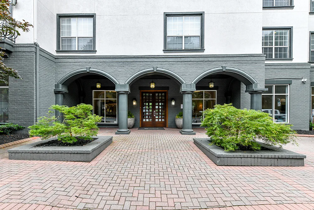 Elegant apartment entrance showcasing classic archways, lush landscaping, and inviting brick pathways.
