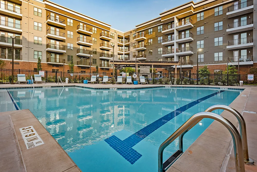 Luxurious apartment complex featuring a sparkling swimming pool surrounded by modern architecture and stylish lounging areas.