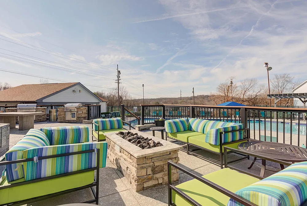 Inviting outdoor patio with colorful seating and a modern fire pit, overlooking a sparkling swimming pool under a clear blue sky.