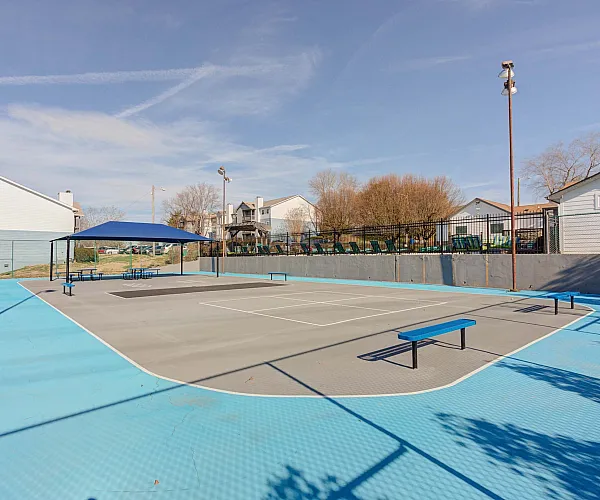 Vibrant recreational area featuring a modern outdoor tennis court with blue accents and shaded seating, ideal for active lifestyle enjoyment.