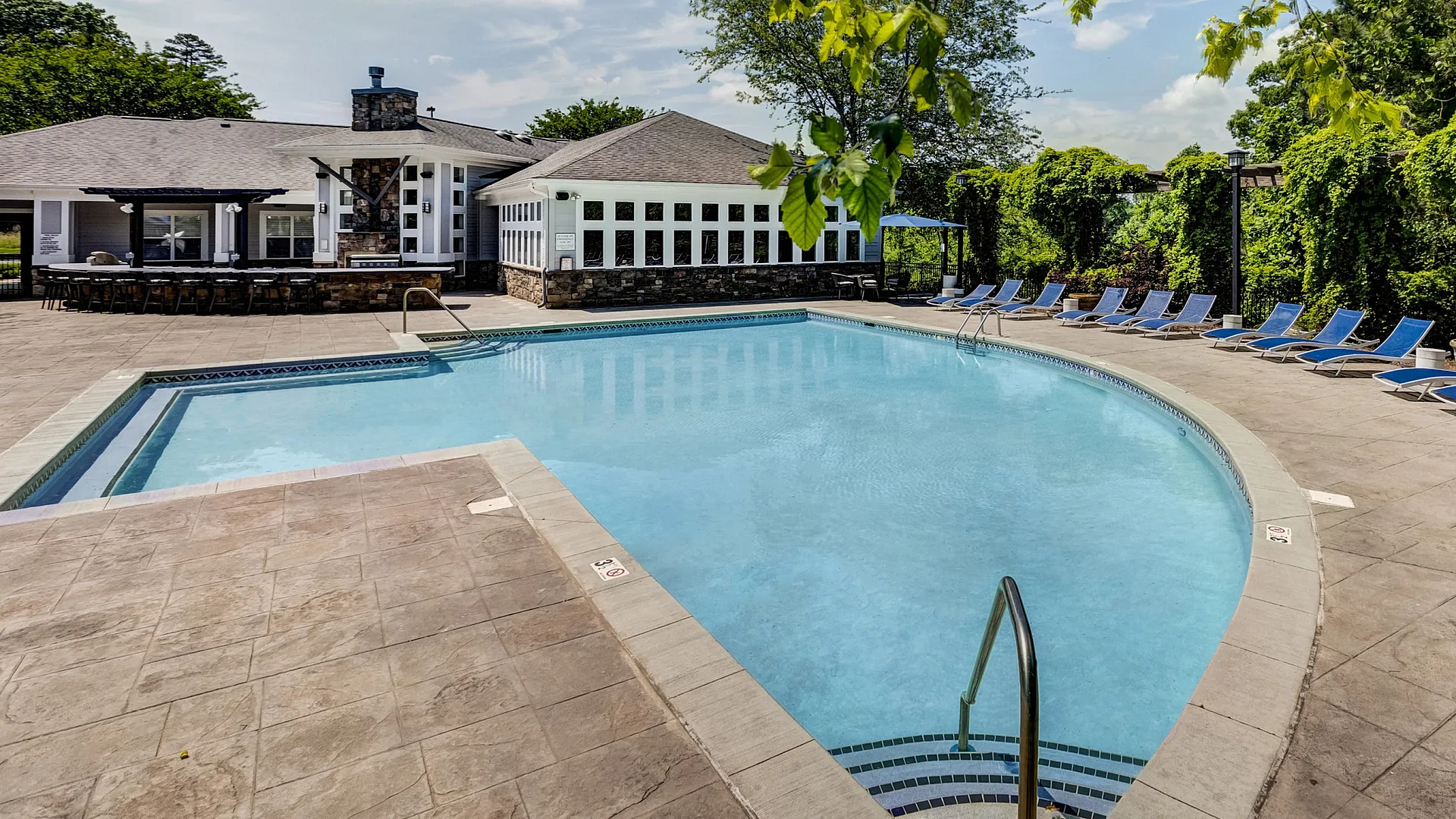 Inviting outdoor pool area with lush greenery, modern clubhouse, and ample lounge seating for relaxation.