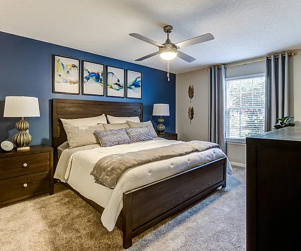 Cozy and elegant bedroom with a king-sized bed, chic decor, ceiling fan, and large window providing natural light.