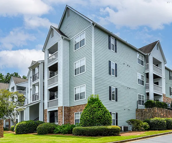 Charming modern apartment building with elegant balconies, surrounded by lush greenery and a well-maintained landscape under a bright sky.