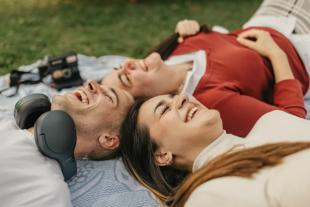 Joyful friends lying on a blanket in a park, enjoying laughter and closeness under the sun.