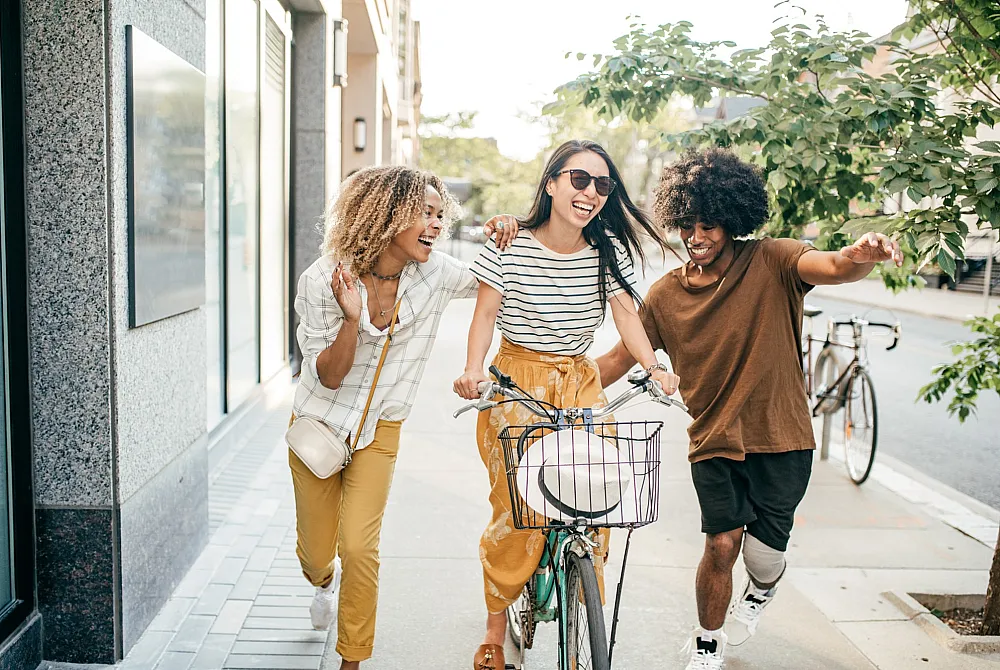 Joyful group of friends sharing a vibrant day out as one rides a bicycle on a lively urban street.