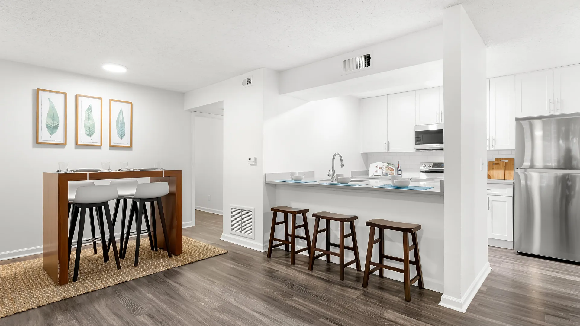 Modern apartment kitchen with sleek stainless steel appliances, stylish bar seating, and elegant wooden flooring.