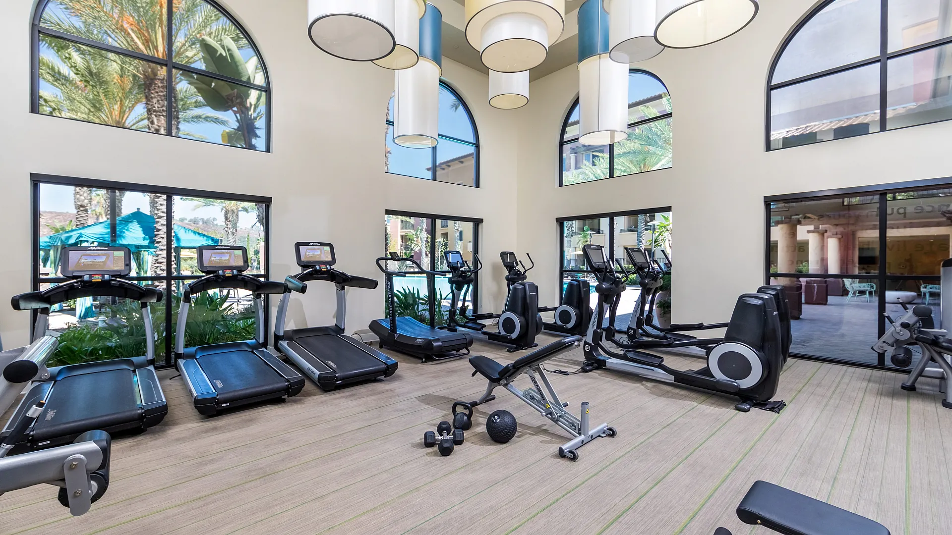 Bright and inviting gym space with modern cardio machines, weight benches, and lush views through large arched windows.
