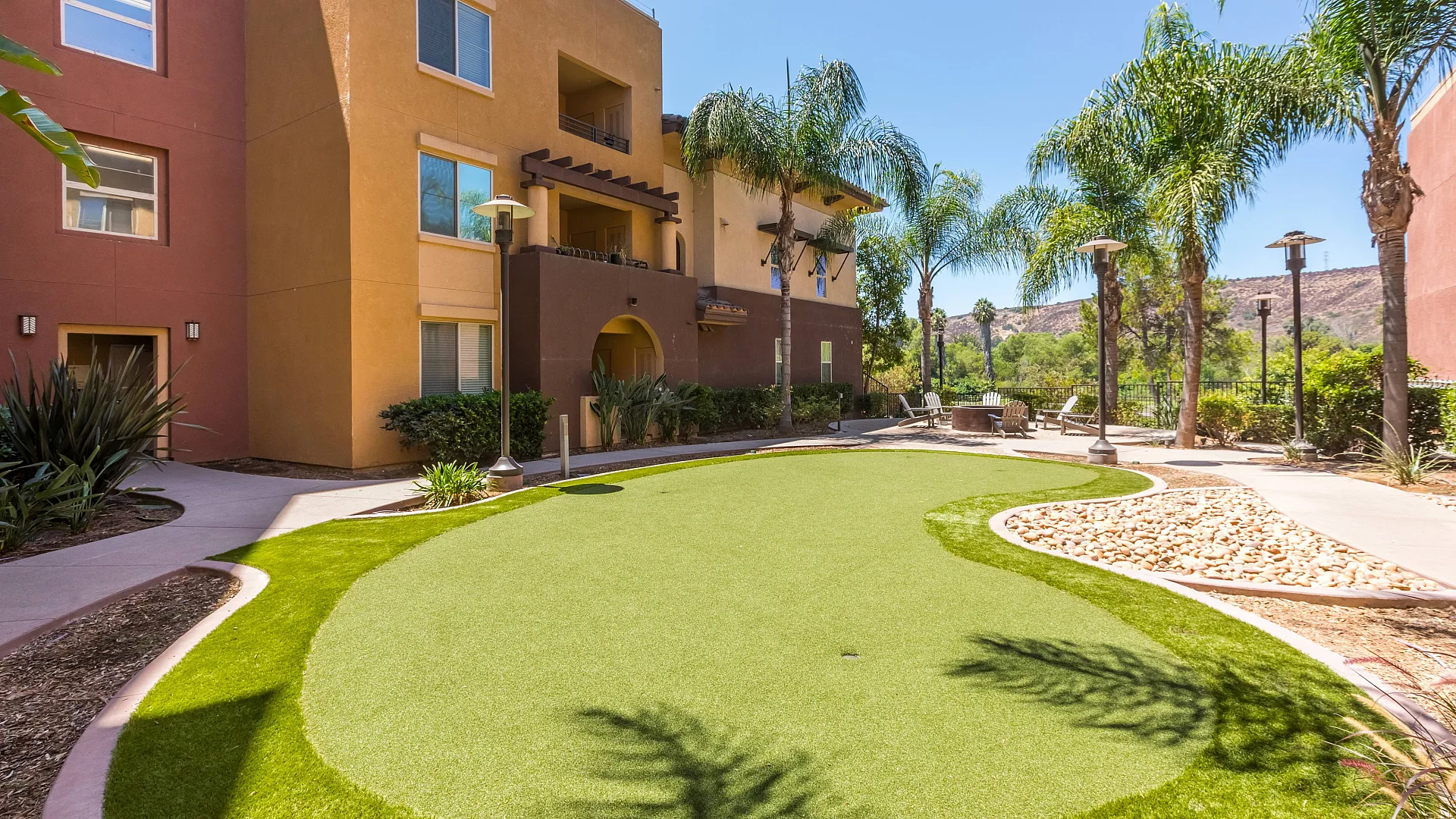 Charming apartment complex featuring vibrant architecture, lush landscaping, and inviting outdoor seating area under sunny skies.