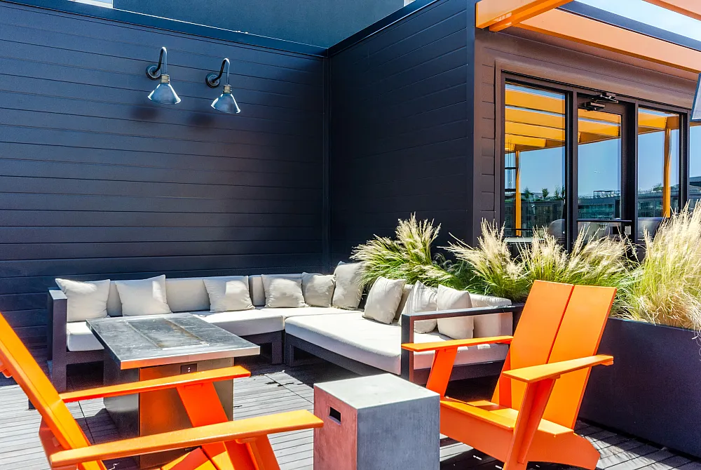 Chic rooftop patio featuring bold orange chairs, a cozy sectional sofa, and lush greenery for ultimate relaxation.