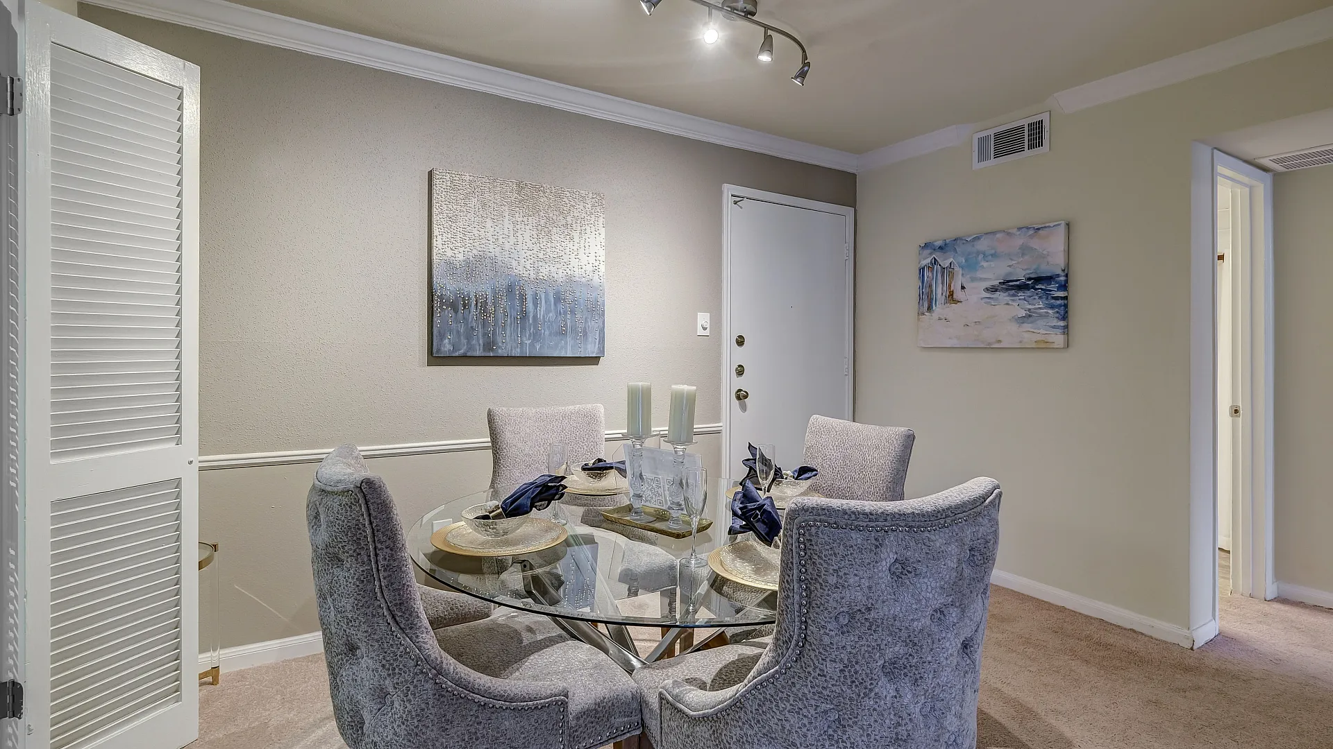 Chic dining area with elegant gray chairs and a glass table, beautifully set for four, under modern track lighting.
