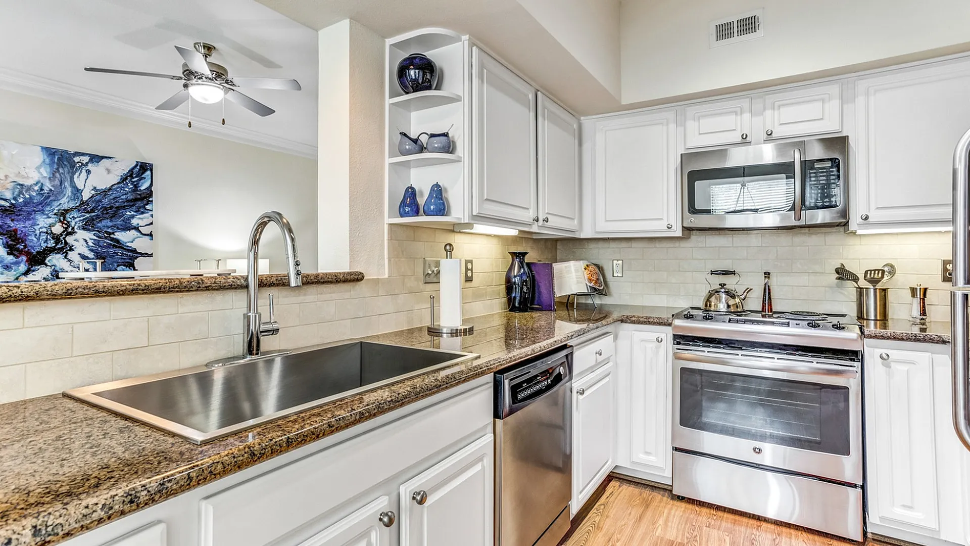 Modern kitchen with stainless steel appliances, gleaming granite countertops, and elegant white cabinetry, highlighted by tasteful decor and a ceiling fan above.