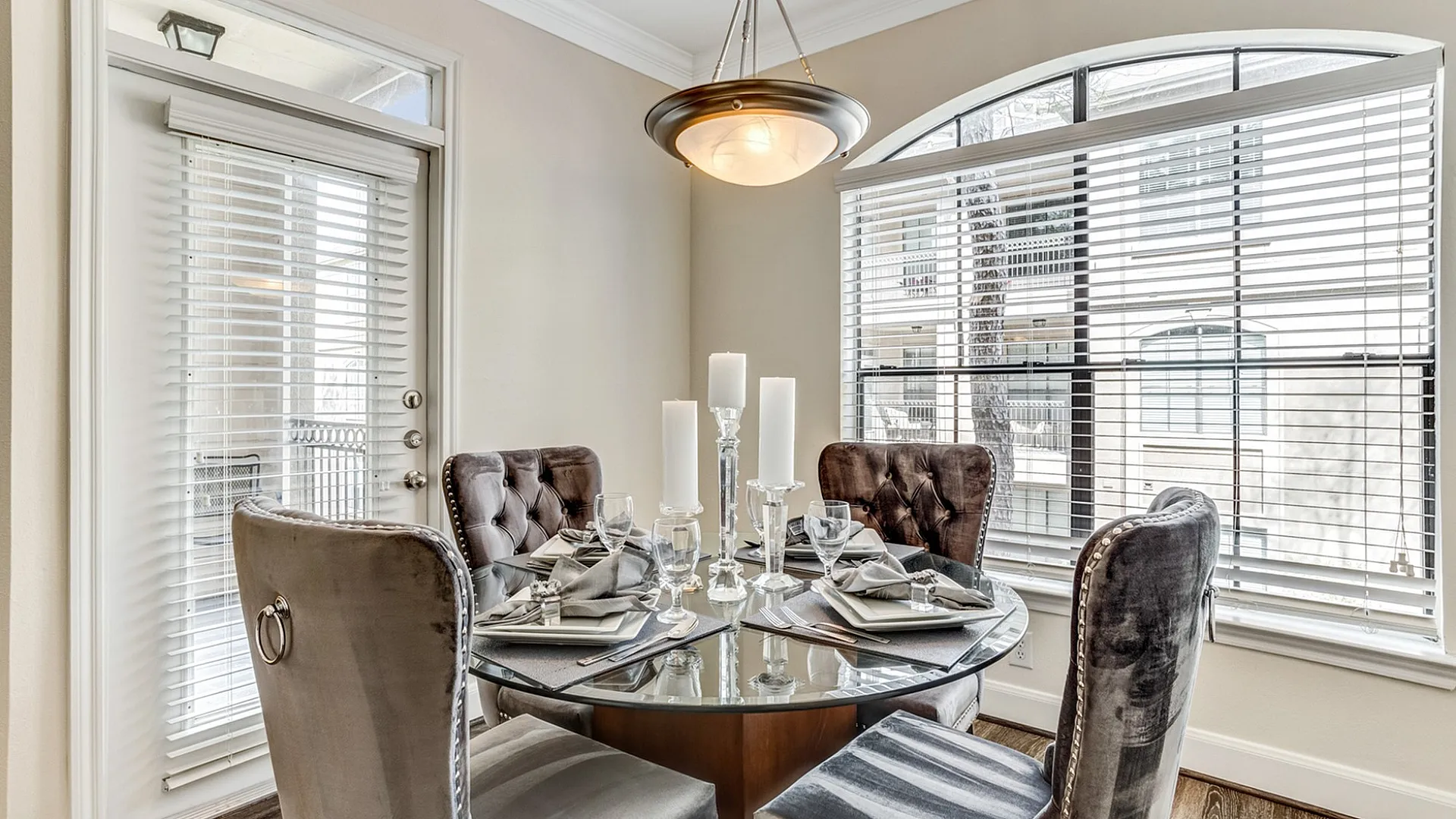 Elegant dining area with plush velvet chairs surrounding a glass table, bathed in natural light from large windows.