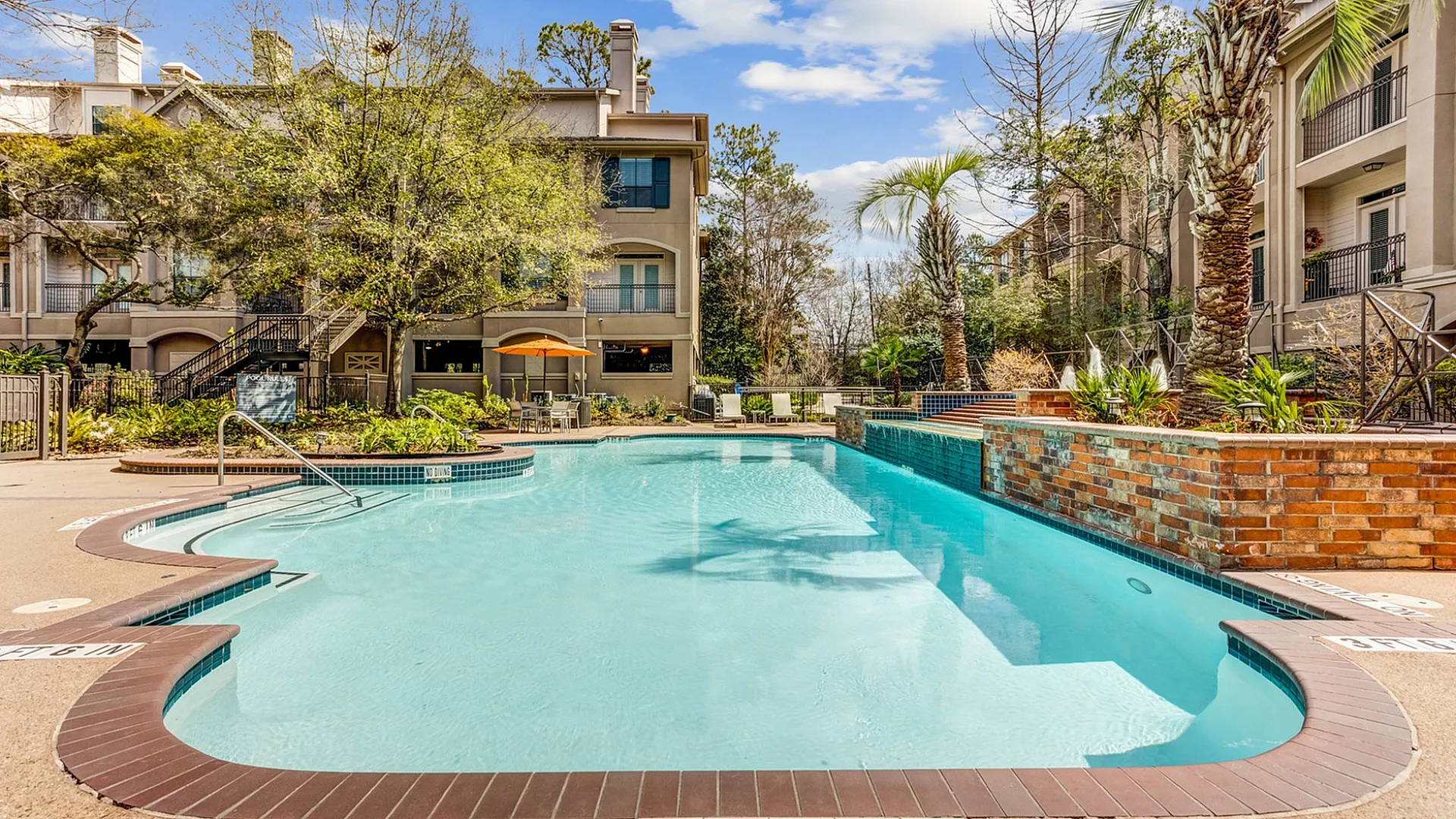 Luxurious apartment complex featuring a sparkling pool, lush greenery, and inviting outdoor seating.