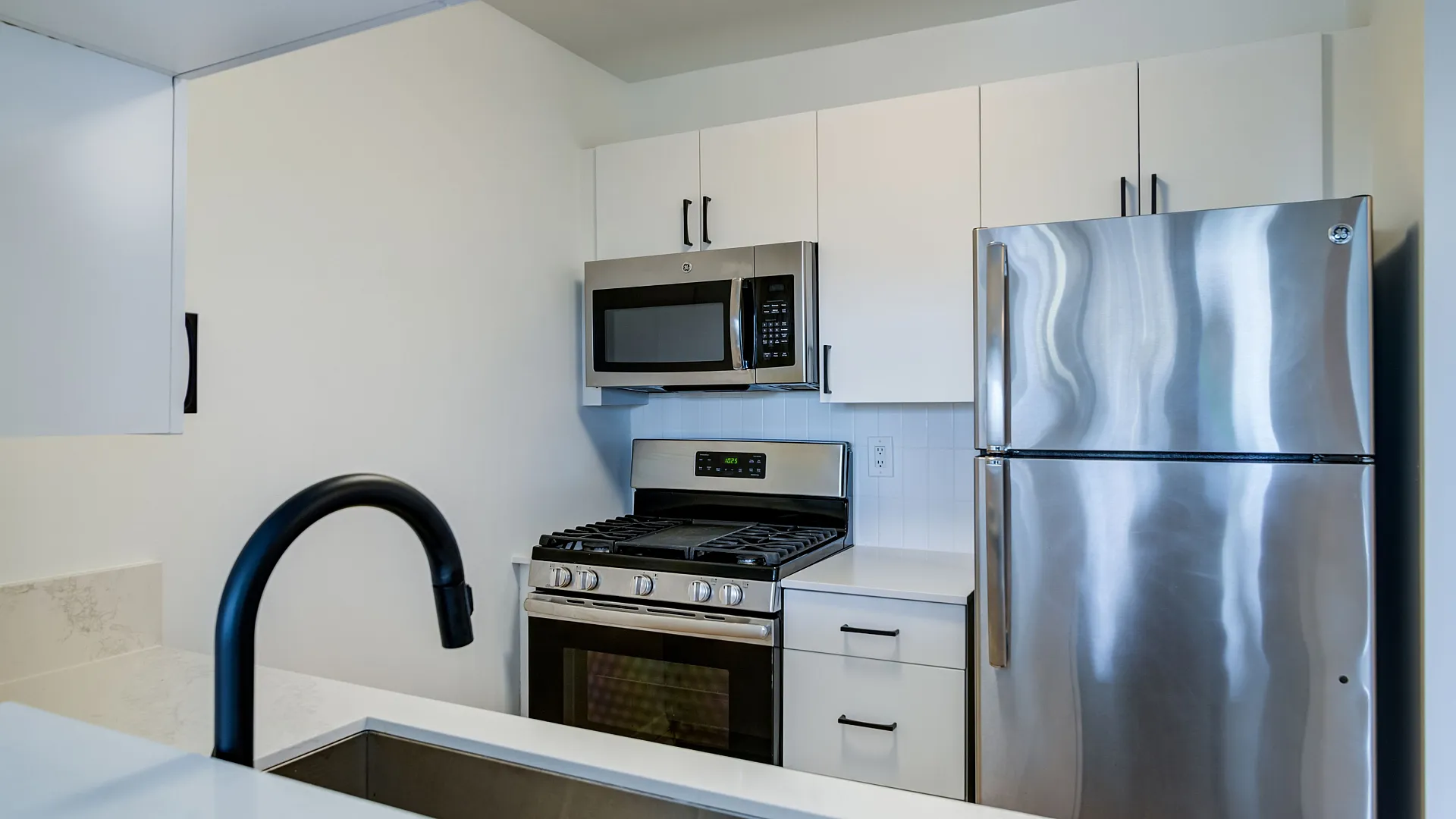 Modern kitchen with sleek stainless steel appliances, white cabinetry, and a stylish black faucet.