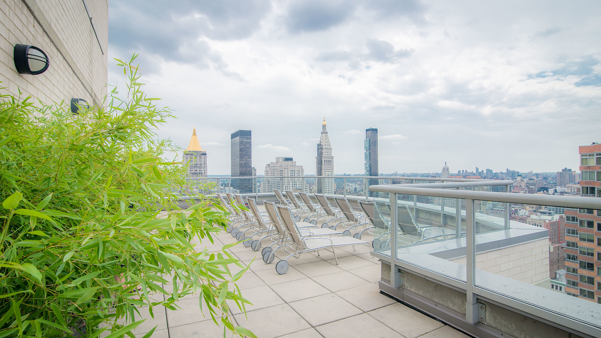 Luxurious apartment rooftop terrace with stylish lounge chairs overlooking a stunning city skyline, complemented by lush green bamboo plants.