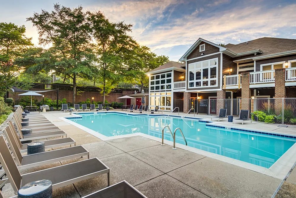 Inviting apartment complex with a pristine outdoor pool, surrounded by stylish lounge chairs and lush greenery, perfect for relaxation.