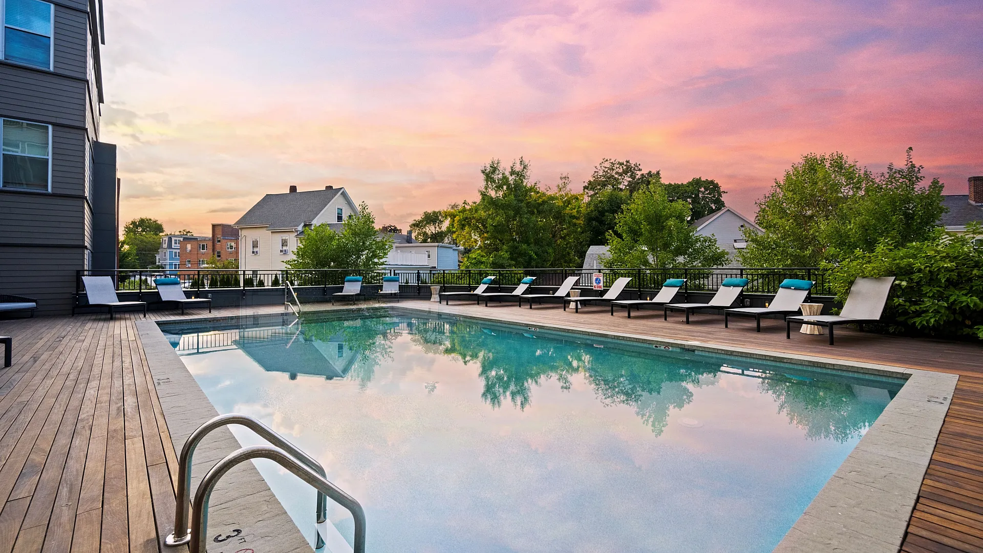 Serene outdoor pool area with stylish lounge chairs against a vibrant sunset sky, perfect for relaxing evenings.