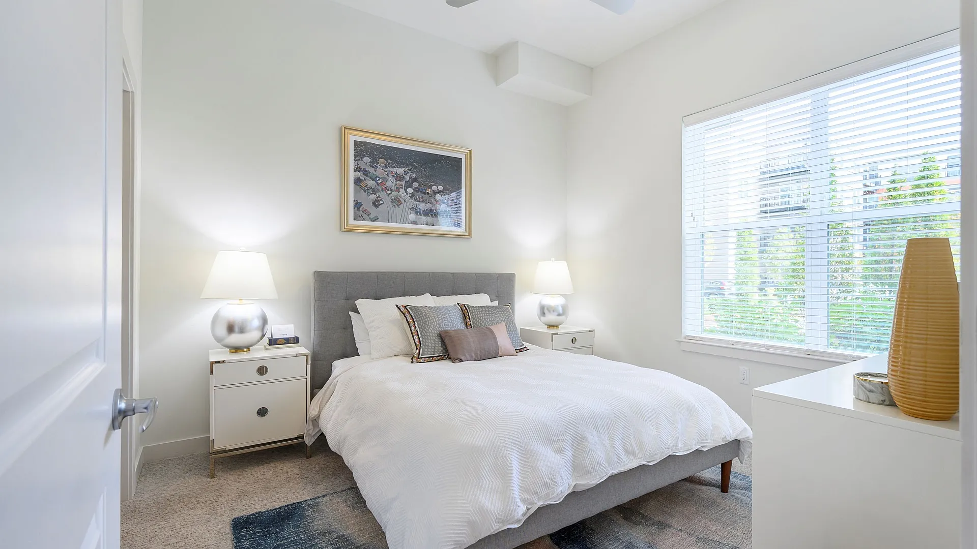 Bright and inviting bedroom with a plush queen-sized bed, modern side tables, elegant lighting, and a large window providing ample natural light.