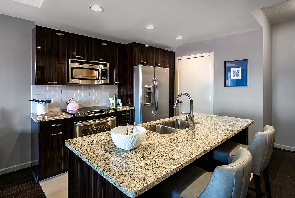 Modern kitchen boasting sleek dark cabinetry, stainless steel appliances, and a granite island with seating.