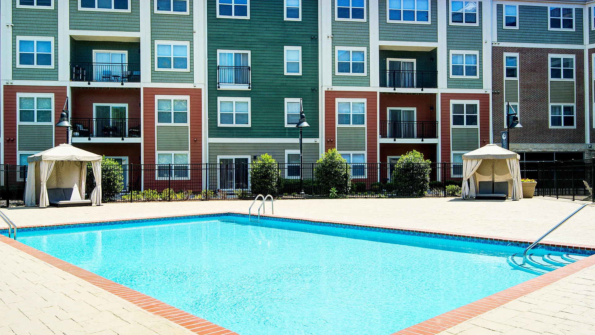 Modern apartment complex with vibrant facade overlooking a pristine swimming pool and elegant cabanas, perfect for relaxation and leisure.
