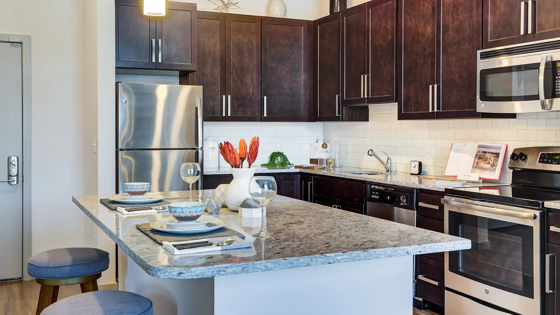 Modern kitchen with elegant dark wood cabinets, sleek stainless steel appliances, and a stylish granite island with seating, perfect for entertaining.