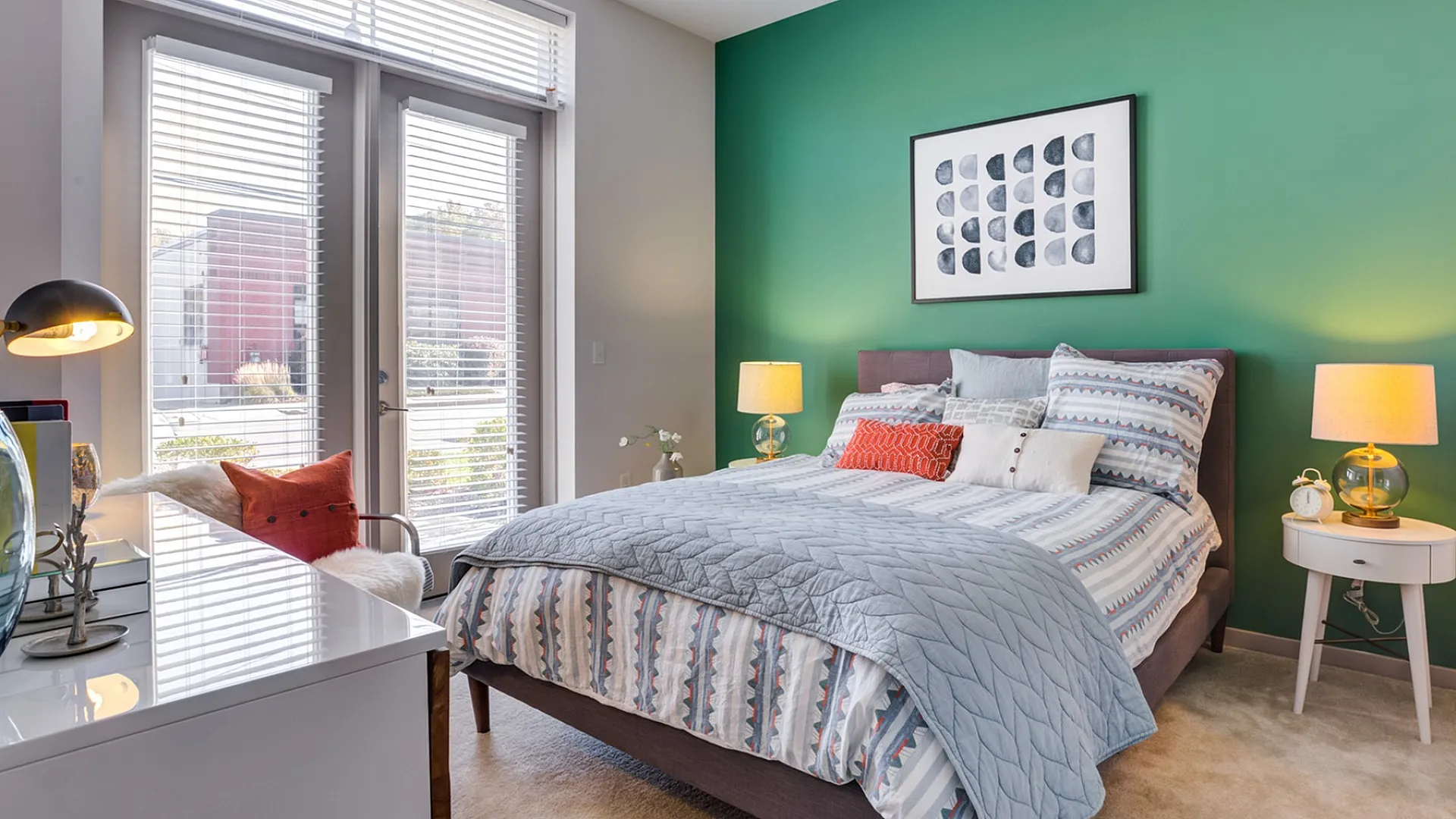 Bright and cozy bedroom featuring a stylish green accent wall, comfortable bed with patterned linens, and ample natural light streaming through large windows.